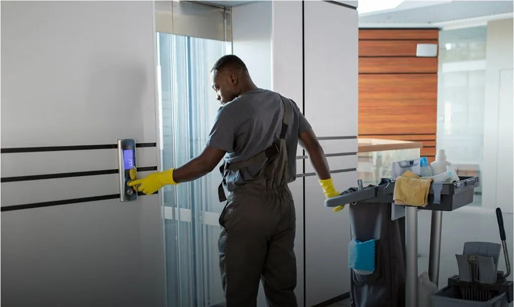 Cleaner disinfecting a door handle in a corridor