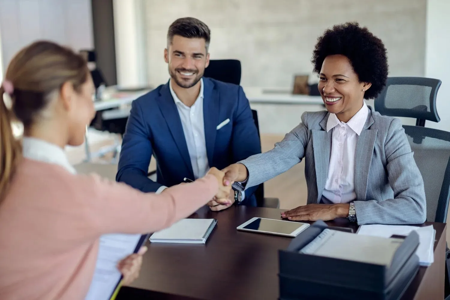 Two partners shaking hands across a desk